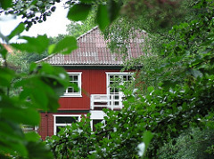 Rotes Holzhaus am Isebekkanal, grünes Blattwerk.