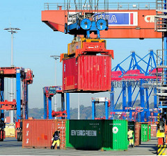 Der Container hängt im Spreader des Bahnportalkrans und wird zum Güterwaggon transportiert.