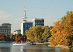 Hamburger Herbst - in Herbstfarben leuchtende Bäume stehen am Alsterufer der Binnenalster - ein Alsterschiff fährt Richtung Lombardsbrücke - im Hintergrund die Hochhäuser an der Esplanade und der Hamburger Fernsehturm / Heinrich-Hertz-Turm, Telemiche
