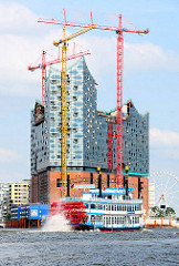 Baukräne an der entstehenden Elbphilharmonie - ein Raddampfer der Hamburger Hafenrundfahrt auf seiner Fahrt durch den Hafen.