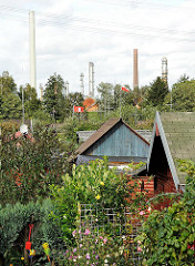 Blick über die Kleingartenparzellen mit Lauben im Hamburger Stadtteil Heimfeld - im Hintergrund Schornsteine des Harburger Industriegebiets an der Süderelbe.