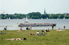 Alsterufer im Stadtteil Hohenfelde - Menschen sonnen sich auf der Wiese - ein Cabrio Alsterschiff macht mit Hamburg Touristen an Bord eine Alsterrundfahrt.
