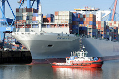Ein Schlepper am Bug des Containerfrachters NYK HELIOS. Das 2013 gebaute Containerschiff hat eine Länge von 365,50m und eine Breite von 48,40m; der Frachter kann 13208 TEU Container transportieren.
