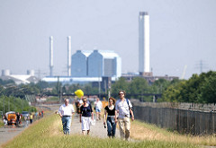 SpaziergängerInnen nutzen die neue Öffnung im Zollzaun am Wilhelmsburger Spreehafen zu einem Spaziergang auf dem Deich - im Hintergrund das Heizkraftwerk Tiefstack in Hamburg Billbrook.