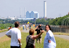 SpaziergängerInnen auf dem Klütjenfelder Hauptdeich in Hamburg Wilhelmsburg / Kleiner Grasbrook; rechts der Zollzaun, im Hintergrund das Heizkraftwerk Tiefstack.