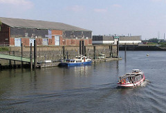 Eine Barkasse fährt aus dem Magdeburger Hafen Richtung Norderelbe - lks. der Liegeplatz des Hafenkapitäns; das Hafenboot liegt am Ponton des Versmannkais - auf der Kaianlage ein grosser Lagerschuppen. (2004)