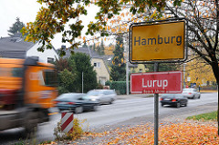 Hamburger Stadtgrenze, gelbes Grenzschild und rotes Stadtteilschild, Autoverkehr mit schnell fahrenden Autos.