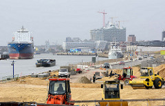 Bauarbeiten am Kirchenpauerkai in der Hamburger Hafencity - Planierraupen schütten Sand auf; ein Binnenschiff fährt elbabwärts - im Hintergrund die Baustelle der Elbphilharmonie.