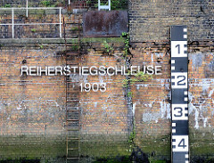 Mauer Reiherstiegschleuse, erbaut 1903; eine rostige Eisenleiter führt ins Wasser - rechts kann die Durchfahrtshöhe bei der Einfahrt in die Schlickschleuse abgelesen werden, die je nach Tide variiert.