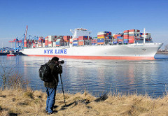 Ein Fotograf hält mit seiner Kamera auf einem Einbeinstativ / Monopod das Ablegen des Containerriesen NYK HELIOS im Hamburger Hafen fest.