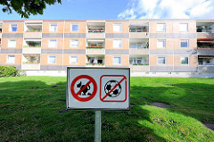 Hinweisschild mit Symbolen - Verbot von Fussball und scheissenden Hunden - zweistöckiger Wohnblock mit Balkons in der Sonne.  Bilder aus dem Hamburger Stadtteil Osdorf.
