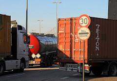 LKW-Stau vor der Zollgrenze in Hamburg Waltershof - ein Schild weist auf die Geschwindigkeitsbegrenzung von 30km/h sowie auf Zoll / Douane hin. Ein Tanklastzug und Auflieger mit Container warten auf die Weiterfahrt.