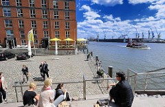 Terrasse in der Sonne an der Grossen Elbstrasse - Blick auf die Elbe und den Hamburger Hafen. Eine Hafenfähre fährt Richtung Finkenwerder - im Hintergrund Kräne der Werft.