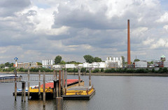 Blick über den Hamburger Wasserweg Reiherstieg zu Raffinerieanlagen in Hamburg Wilhelmsburg - Öltanks und hoher Fabrikschornstein - rechts der Wasserturm von Hamburg Wilhelmsburg.