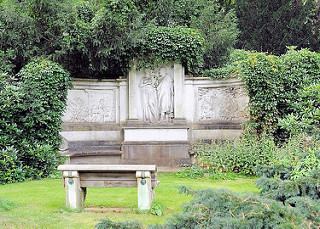 bildarchiv-hamburg.com: Foto Grabstein mit figrlichen Relief mit Efeu  bewachsen - steinerne Ruhebank vor dem Grab.