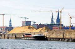 Arbeitsschiff an der Kaianlage des Versmannkai im Baakenhafen - Kirchtürme der Hansestadt Hamburg im Hintergrund.