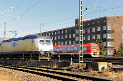 Fahrender Metronomzug und  S - Bahn auf den Gleisen auf der Veddel - Bahnstrecke am Wohngebiet; Klinkerhäuser auf der Hamburger Veddel.