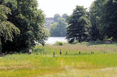 Fussgänger und Jogger auf der Holzbrücke über die Feuchtwiese im Harburger Stadtpark - im Hintergrund der Aussenmühlenteich.