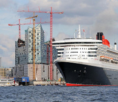 Das Kreuzfahrtschiff Queen Mary läuft aus dem Hamburger Hafen aus - im Hintergrund die Baustelle der Elbphilharmonie; hohe Baukräne.