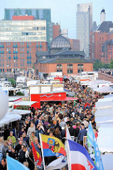 Sonntag früh in Hamburg - der Altonaer Fischmarkt als Sehenswürdigkeit der Hansestadt - dicht gedrängt gehen die Besucher zwischen den Marktständen - im Hintergrund die historische Fischauktionshalle und Industriearchitektur / Büroarchitektur in der