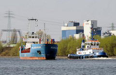 Das Küstenmotorschiff WILSON RUHR fährt in den Reiherstieg ein - der Kümo wird von einem Hafenschlepper überholt. Im Hintergrund Industriegebäude in Hamburg Wilhelmsburg.