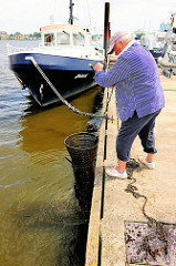 Eine ausgelegte Metallreuse wird von dem Fischer aus dem Wasser geholt.