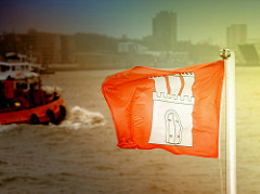 Flagge der Freien und Hansestadt Hamburg flattert im Wind - Silhouette der Stadt - Foto aus dem Hamburger Hafen / Elbe.
