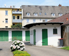 Garagen mit grünen Holztüren - halbrunder Schuppen - Wohnblocks im Hintergrund, Nachkriegsarchitektur.