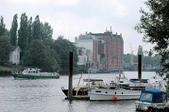 Villa Hintzpeter an der Billwerder Bucht zwischen Bäumen - Sportboothafen; ein Schiff des Hamburger Zolls fährt Richtung Norderelbe.