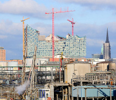 Erdölraffinerie im Hamburger Hafen - Kleiner Grasbrook - im Hintergrund die Baustelle der Elbphilharmonie mit Baukränen und der eingerüstete Kirchtumr der Nikolaikirche.