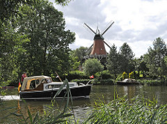 Reitbrooker Mühle am Ufer der Dove-Elbe - Windmühle mit Flügeln in Hamburg - Schilf am Flussufer - Motorboot in Fahrt.