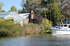 Treibhäuser, Glashäuser am Ufer der Dove Elbe in den Vierlanden, Stadtteil Curslack - Bezirk Hamburg Bergedorf; ein Sportboot in Fahrt.