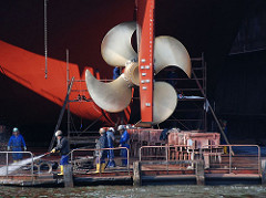 Werftarbeiter auf einem Schwimmdock am Steuerruder eines Frachtschiffs - Werftarbeit auf Hamburg Steinwerder.