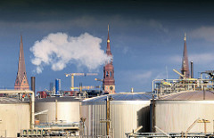 Erdöltanks auf dem Kleinen Grasbrook im Hamburger Hafen - im Hintergrund Kirchtürme der St. Petrikirche, St. Katharinenkirche und der St. Jacobikirche - weisser Rauch steigt aus einem Schornstein.