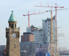 Uhr und Pegelturm der St. Pauli Landungsbrücken; Baukräne und Bauvorhaben der Elbphilharmonie mit entstehender moderner Glasfassade.