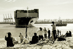 Der Frachter CMA CGM CARMEN läuft in den Hamburger Hafen ein - das Containerschiff wendet auf der Elbe; Zuschauer am Elbstrand bei der Strandperle in Hamburg Othmarschen.