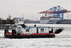 Schubschiff im Eis der Elbe im Hamburger Hafen - dunkle Abgaswolke - Dieselmotor; im Hintergrund das Terminal Tollerort.