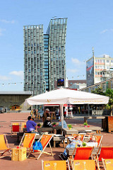 Beachclubfeeling auf dem Millerntorplatz - Liegestühle und Sonnenschirme in der Sonne - im Hintergrund das Hochhaus Tanzende Türme. Fotografien aus dem Hamburger Stadtteil St. Pauli.