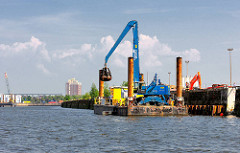 Ein Kran baggert von einem Ponton aus den Baakenhafen aus. Motive aus dem Hamburger Stadtteil Hafencity.