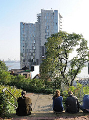 Blick vom Elbberg zum Neubau-Hochhaus am Elbufer bei der Großen Elbstrasse, Hamburg Altona Altstadt. Menschen sitzen in der Sonne auf der Treppe.