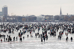 Alstereisvergnügen auf dem Eis der zugefrorenen Aussenalster - Menschen auf dem Eis, Silhouette von Hamburg - grauer Wintertag in der Hanstestadt.
