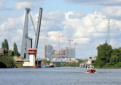 Blick vom Reiherstieg zur Baustelle der Elbphilharmonie; ein Sportboot fährt Richtung Rethe, die Reiherstiegklappbrücke ist hochgeklappt.