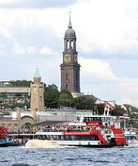 Blick über die St. Pauli Landungsbrücken zur St. Michaeliskrirche in der Neustadt Hamburgs. Auf der Elbe fährt eine vollbesetzte Hafenfähre Richtung Altona.