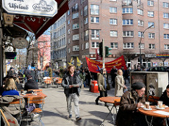 Demonstrationszug vom Hamburger Ostermarsch in der Langen Reihe in Hamburg St. Georg - Demonstranten auf der Strasse - Gäste in Strassencafes in der Sonne.