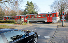 Geschlossene Bahnschranken am Harksheider Weg in Quickborn; wartendes Auto, fahrender AKN-Zug.