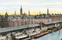 Blick auf die Kaianlagen im Sandtorhafen - Sandtorkai im historischen Hamburger Hafen - Dampfschiffe liegen am Kai, sie werden über Kräne be- und entladen. Auf der Wasserseite Kähne und Schuten - im Hintergrud die Speichergebäude der Hambu