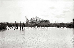 Im Seehafen wird die Fracht eines Kohlenfrachters gelöscht - ein Elbkahn liegt längsseits, der Laderaum ist aufgedeckt. Hinter den Holzdalben sind die Halbportalkräne am Kai zu erkennen. (ca. 1938)