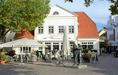 Am Markt von Neustadt in Holstein, historisches Wohnhaus / Geschäftshaus, jetzt Café / Restaurant mit Aussengastronomie; Bronzeskulptur Fischer von Serge Mangin.