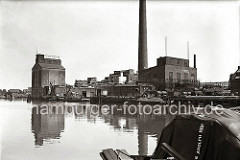 Fabrikationsanlage mit Silo und hohem Schornstein der "Thörl's Vereinigte Harburger Ölfabriken AG" im Harburger Überwinterungshafen. Fässer liegen auf dem Kai, eine Schute wird über eine Kippvorrichtung beladen. (ca. 1938)