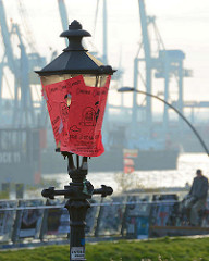 Historische Laterne an der St. Pauli Hafenstrasse mit Werbung verklebt - Kräne im Hamburger Hafen, Elbe.